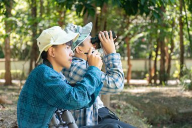 Yaz kampı sırasında tropikal ormanda kuş gözlemlemek için dürbün kullanan Asyalı çocuklar, sınıfın dışında yaşayan canlıları, vahşi hayvanları ve böcekleri öğrenme fikri.