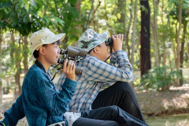 Yaz kampı sırasında tropikal ormanda kuş gözlemlemek için dürbün kullanan Asyalı çocuklar, sınıfın dışında yaşayan canlıları, vahşi hayvanları ve böcekleri öğrenme fikri.