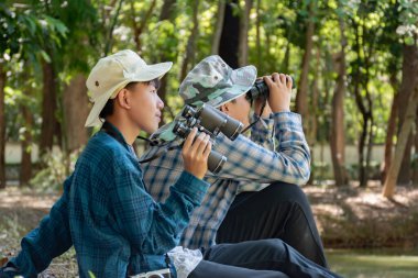 Yaz kampı sırasında tropikal ormanda kuş gözlemlemek için dürbün kullanan Asyalı çocuklar, sınıfın dışında yaşayan canlıları, vahşi hayvanları ve böcekleri öğrenme fikri.