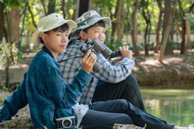 Yaz kampı sırasında tropikal ormanda kuş gözlemlemek için dürbün kullanan Asyalı çocuklar, sınıfın dışında yaşayan canlıları, vahşi hayvanları ve böcekleri öğrenme fikri.