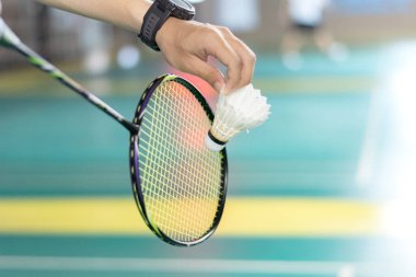 Badminton oyuncusu, raketi ve beyaz kremalı mekikçiyi sahanın diğer tarafına götürmeden önce kalenin önünde tutuyor..
