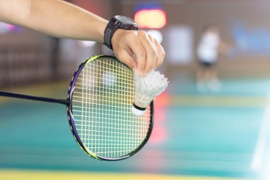Badminton oyuncusu, raketi ve beyaz kremalı mekikçiyi sahanın diğer tarafına götürmeden önce kalenin önünde tutuyor..