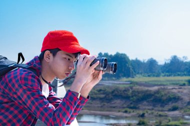Asyalı bir çocuk, kep ve ekose gömlek giyiyordu. Dürbünle nehrin üzerindeki köprüde dikilip bakıyordu. Doğal ortamın tadını çıkarıyor ve yabani hayatı merakla izliyor..