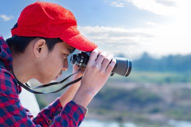Asyalı bir çocuk, kep ve ekose gömlek giyiyordu. Dürbünle nehrin üzerindeki köprüde dikilip bakıyordu. Doğal ortamın tadını çıkarıyor ve yabani hayatı merakla izliyor..