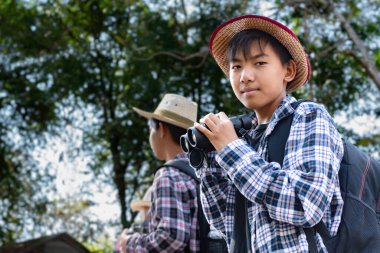 Asyalı çocuklar grup halinde durup dürbünle bakıyorlar ve parkta vahşi hayvan görmek için bekliyorlar. Doğal ortamın tadını çıkarıyorlar ve yabani hayatı merakla izliyorlar..
