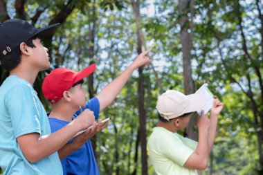 Asyalı öğrenciler, ellerinde inclino metre ölçü kağıdı tutarak ve ağaçların yüksek seviyesini ölçerek ve bilgileri taplet 'e kaydederek okullarının botanik bahçesindeki yüksek seviyedeki ağaçları inceliyorlar..