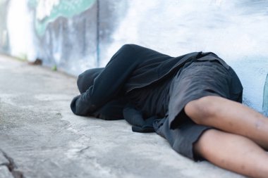 Siyah başörtüsü takan Asyalı bir genç, kötü davranışlarından dolayı ebeveynleri tarafından cezalandırıldıkları için binanın duvarında uyur ki bu günümüz toplumunda bir sorundur, evsiz insanlar konsepti..