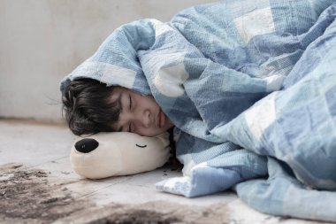 Asyalı evsiz çocuk, kirli zemin ve duvarları toz ve kirle dolu olan bir binanın zemininde ve duvarlarında battaniyelerle yatıyordu, yumuşak odak, gençlerin yaşam tarzı sorunları kavramı..