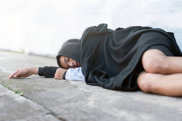 Asian teenager wearing black headscarves sleep on the outside wall of a building as they are punished by their parents for bad behavior, which is a problem in today's society, homeless people concept.