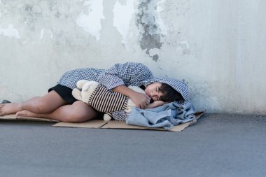 Siyah kapüşonlu Asyalı genç kirli zeminde ve terk edilmiş bir binanın dağınık duvarında uyuyor, üzgün görün, yumuşak odaklan, evsiz konsepti, hapsedilme ve gençlerin gözaltına alınması kavramı.