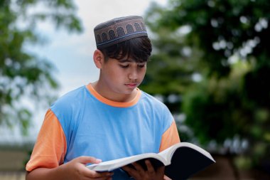 Genç Müslüman ya da İsalmik çocuk bir kitap tutuyor ve parkta okuyor..
