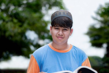 Genç Müslüman ya da İsalmik çocuk bir kitap tutuyor ve parkta okuyor..