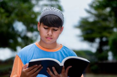 Genç Müslüman ya da İsalmik çocuk bir kitap tutuyor ve parkta okuyor..