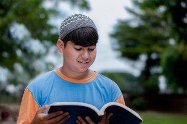 Genç Müslüman ya da İsalmik çocuk bir kitap tutuyor ve parkta okuyor..