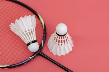 Badminton spor malzemeleri, raket ve beyaz krem rengi mekiks tüyü top kırmızı zeminde, yumuşak ve seçici odaklanma.