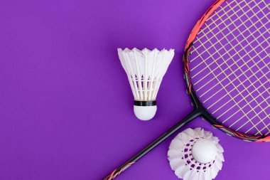 Badminton spor ekipmanları, raket ve beyaz krema, menekşe zemininde tüy yumağı, yumuşak ve seçici odaklanma.