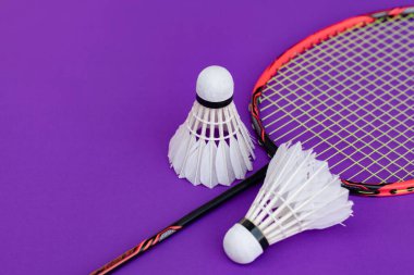 Badminton spor ekipmanları, raket ve beyaz krema, menekşe zemininde tüy yumağı, yumuşak ve seçici odaklanma.