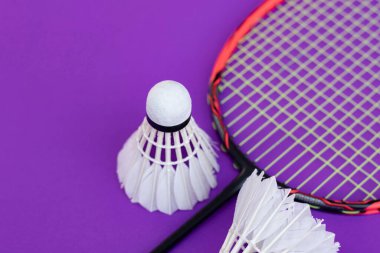 Badminton spor ekipmanları, raket ve beyaz krema, menekşe zemininde tüy yumağı, yumuşak ve seçici odaklanma.