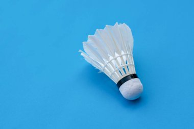 Badminton spor malzemeleri, raket ve beyaz krem rengi, mavi zeminde tüylü top, yumuşak ve seçici odaklanma.