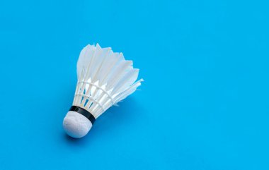 Badminton spor malzemeleri, raket ve beyaz krem rengi, mavi zeminde tüylü top, yumuşak ve seçici odaklanma.