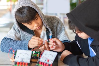 Çocuklar, fizik bilimi dersinde küçük bir elektrik sayacı ve küçük bir fener ampulü kullanarak elektrik devreleri üzerinde deneyler yapıyorlar.