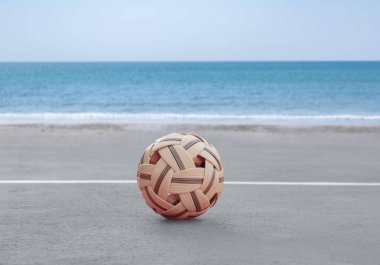 Sepak, kumsal sahasının kum zemininde topu, bulanık mavi gökyüzü ve deniz arka planı, Güneydoğu Asya ülkelerindeki eğlence aktivitesi ve açık hava sporları konsepti.