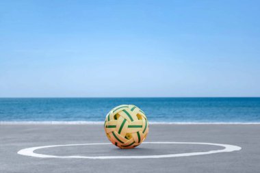 Sepak, kumsal sahasının kum zemininde topu, bulanık mavi gökyüzü ve deniz arka planı, Güneydoğu Asya ülkelerindeki eğlence aktivitesi ve açık hava sporları konsepti.