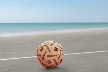 Sepak, kumsal sahasının kum zemininde topu, bulanık mavi gökyüzü ve deniz arka planı, Güneydoğu Asya ülkelerindeki eğlence aktivitesi ve açık hava sporları konsepti.