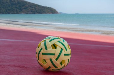 Sepak, kumsal sahasının kum zemininde topu, bulanık mavi gökyüzü ve deniz arka planı, Güneydoğu Asya ülkelerindeki eğlence aktivitesi ve açık hava sporları konsepti.