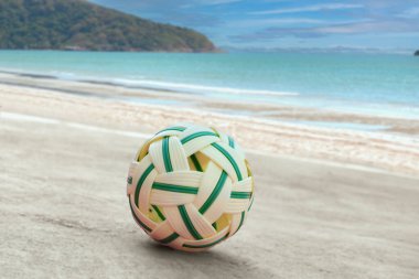 Sepak, kumsal sahasının kum zemininde topu, bulanık mavi gökyüzü ve deniz arka planı, Güneydoğu Asya ülkelerindeki eğlence aktivitesi ve açık hava sporları konsepti.