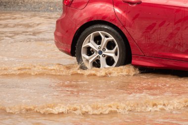 Şiddetli yağmurun yol açtığı sel baskınında su basmış bir yolda giden araba..