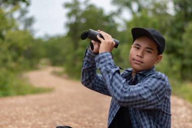 Dürbünlü genç adam güneşli bir günde ormanı keşfediyor, açık hava macerası ve vahşi hayatı gözlemliyor..