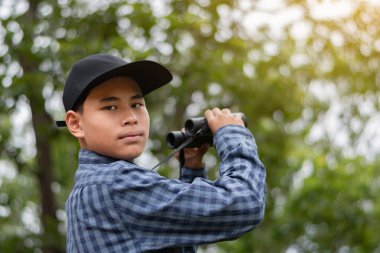 Dürbünlü genç adam güneşli bir günde ormanı keşfediyor, açık hava macerası ve vahşi hayatı gözlemliyor..