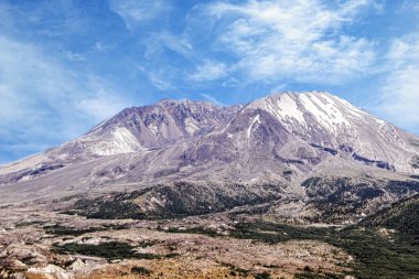 Görüntü, St. Helens Dağı 'nın engebeli arazisini gösteriyor. Volkanik yaralar, kayalık yamaçlar ve parlak mavi gökyüzü altındaki kar parçaları doğal güzelliği ve yıkımı simgeliyor.