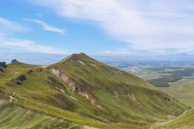 Massif du Sancy yeşil yamaçlarla çevrili, açık mavi bir gökyüzü ve ufukta uzanan geniş bir vadi; Auvergne, Fransa