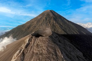 Guatemala 'daki Volkan de Fuego ve Acatenango volkanlarının hava görüntüsü aktif kraterden yükselen dumanla birlikte. Dramatik volkanik manzara bulutların üzerinde, açık mavi gökyüzünün altında yükseliyor. Merkez Ame 'nin saf gücünü ve güzelliğini gözler önüne seriyor.