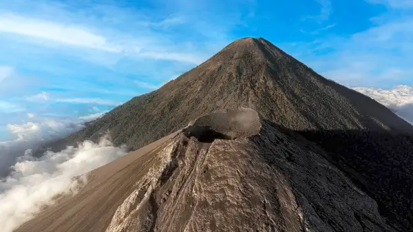Guatemala 'daki Volkan de Fuego ve Acatenango volkanlarının hava görüntüsü aktif kraterden yükselen dumanla birlikte. Dramatik volkanik manzara bulutların üzerinde, açık mavi gökyüzünün altında yükseliyor. Merkez Ame 'nin saf gücünü ve güzelliğini gözler önüne seriyor.