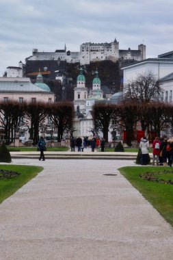 Salzburg, Avusturya - 30 Kasım 2019: Mirabell Sarayı ve Salzburg Katedrali 'nin önündeki arka planda Hohensalzburg Kalesi olan bahçelerde yürüyüş yolu.