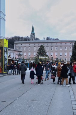 Salzburg, Avusturya - 30 Kasım 2019: Avusturya 'da bir sonbahar günü tarihi binalarla eski bir kasabadaki bir Noel pazarının önünde yürüyen insanlar.