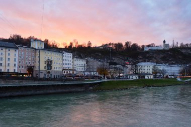 Salzburg, Avusturya - 30 Kasım 2019: Avusturya 'nın Salzburg kentinde bir sonbahar öğleden sonrasında Salzach nehrinin yanındaki binaların üzerinde güzel renkli gökyüzü.