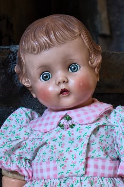 Mavi gözlü, pembe yanaklı, pembe çiçekli beyaz bir elbise giyen antika bir bebeğin yüzü..
