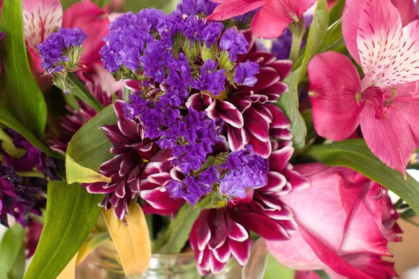 Bouquet of purple and pink flowers with green leaves in a vase.