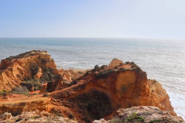 Bright colorful cliffs at Praia do Carvoeiro, a beach next to the Atalantic Ocean on a warm winter day in Portugal.