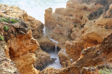 Small trickle of water running over a rocky area next to the Atalantic ocean at Praia do Carvoeiro, a beach in Portugal on a warm winter day.