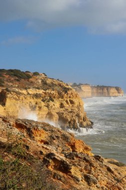 Water splashing on orange cliffs on a sunny, windy winter day in Carvoeiro, Portugal.