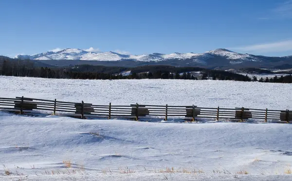 Wooden fence next to the highway with the Bighorn Mountains in the distance on a sunny winter day in Wyoming.