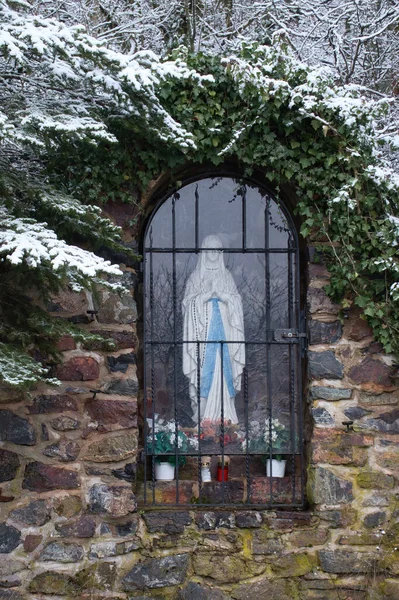 Falkenstein, Germany - January 31, 2021: Statue in a window surrounded by plants covered in snow on a winter day in Rhineland Palatinate next to Falkenstein castle ruins.