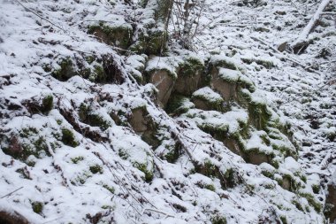Pile of rocks covered in snow on a hill in the Palatinate Forest of Germany on a cold winter day.
