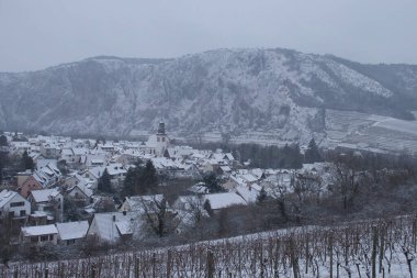 Bad Munster am Stein-Ebernburg, Germany - Febryary 8, 2021: Houses and church in Bad Munster in front of Rotenfels covered in snow on a cold, grey winter day in Rhineland Palatinate, Germany.