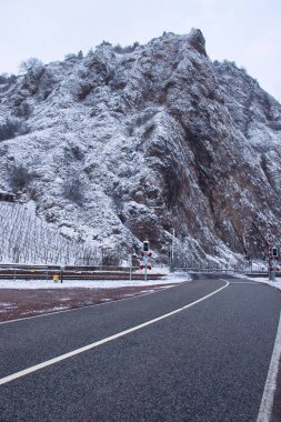 Road leading to railroad crossing in front of hill in Rotenfels on a snowy winter day in Bad Kreuznach, Germany.